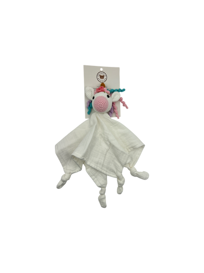 A white muslin comforter blanket featuring a crocheted unicorn head with a pink spiral nose, rainbow mane, and small pink and blue horns, attached to a white paper header card.